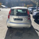 Silberner Suzuki Splash mit CH-Aufkleber auf Parkplatz, umgeben von herbstlicher Landschaft und Gebirge im Hintergrund.