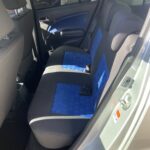 Rückbank eines Autos mit blauen Sitzpolstern, geöffnete Tür, Innenansicht bei Tageslicht.