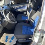 Innenansicht eines Autos mit blau-schwarzen Vordersitzen und Fußmatte im Sonnenlicht.
