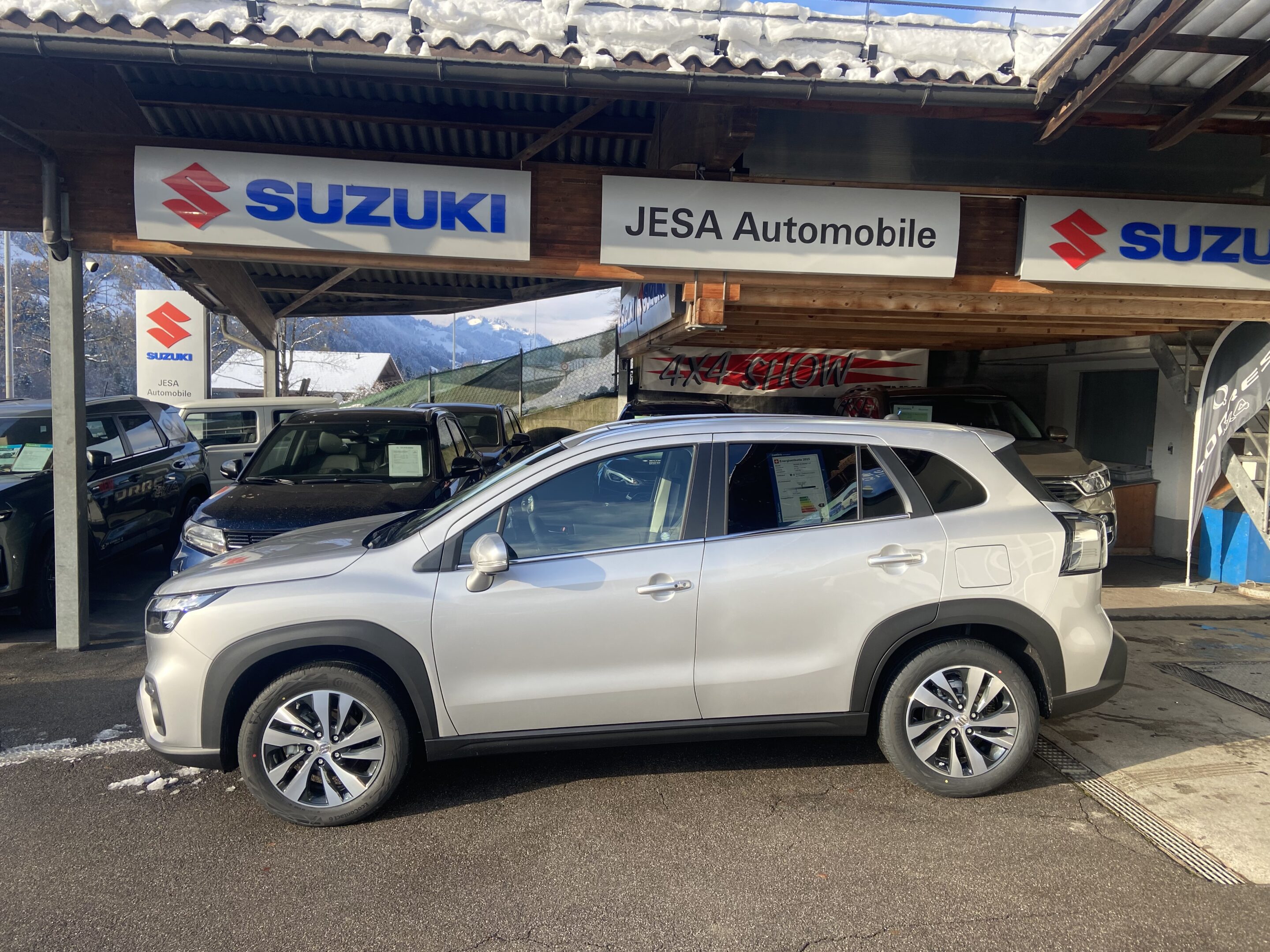 Silberner Suzuki SUV bei JESA Automobile Händler vor Bergkulisse im Freien ausgestellt.