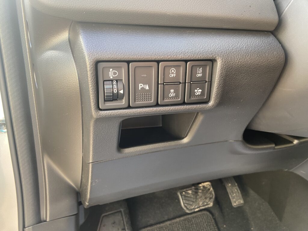 Autoinnenraum-Tastenleiste mit Steuerknöpfen für Scheinwerfer und Assistenzsysteme nahe Fahrerbereich.