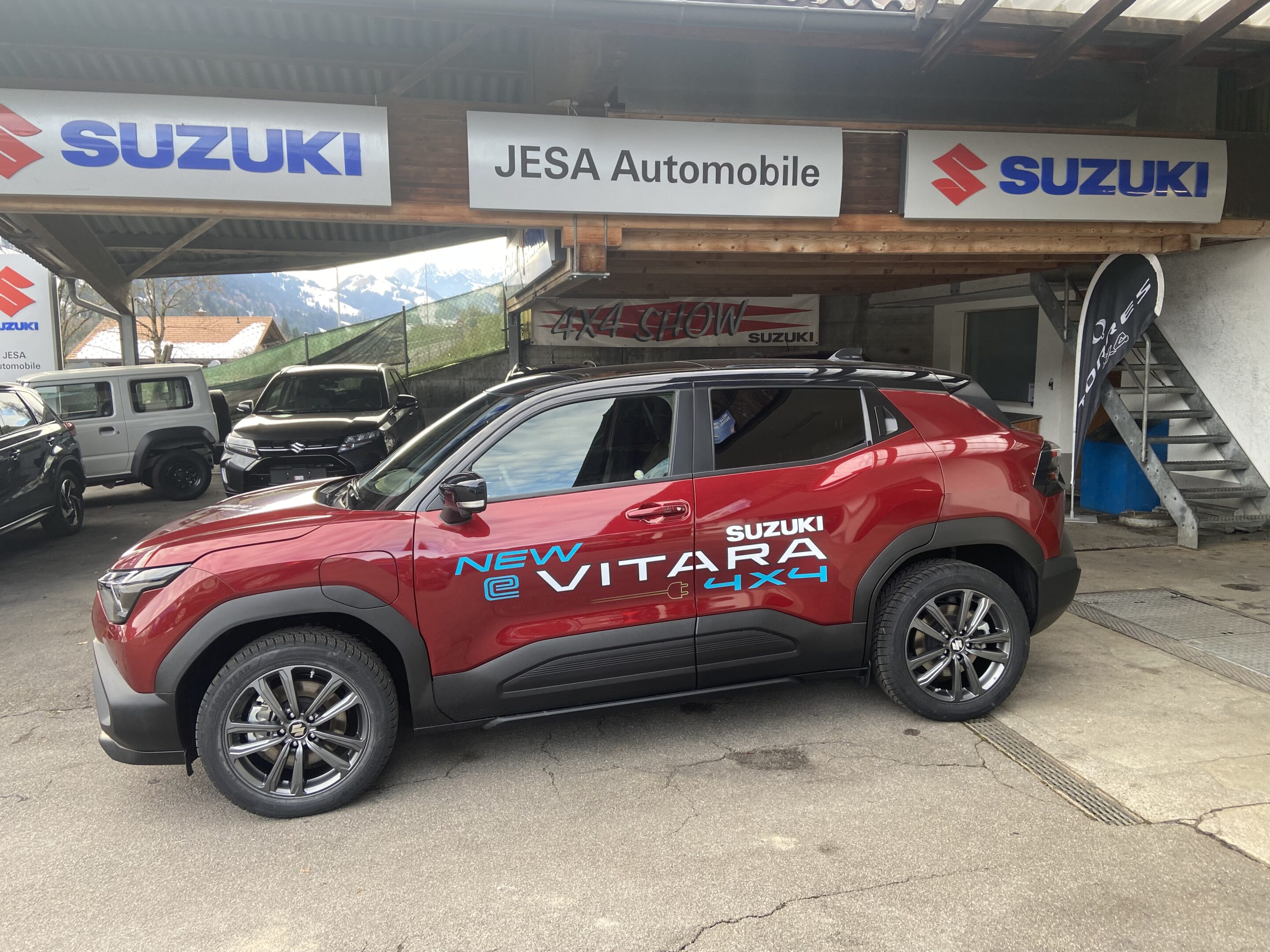 IMG_0600 Roter Suzuki eVitara 4x4 geparkt vor Jesa Automobile mit Suzuki-Schildern im Hintergrund.