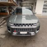 Graues SUV Torres Modell, geparkt vor einer Garage unter einem Holzdach.