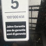 5 Jahre Garantie oder 100.000 km auf einem regennassen Fahrzeugschild in mehreren Sprachen.