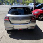 Silberner Suzuki Swift Hybrid auf Parkplatz, umgeben von grüner Landschaft und anderen Autos.
