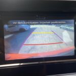 Rückfahrkameraansicht eines Autos mit Sicherheitslinien auf Display, Hinweis zur Sicherstellung der Sicherheit beim Zurücksetzen.