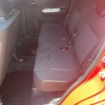 Rückbank eines Autos mit grauer Polsterung, offene Tür, rotes Äußeres, Tageslicht, moderner Innenraum, geräumiger Sitz.