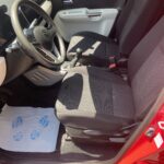 Roter Suzuki Innenraum, Vordersitze und Lenkrad sichtbar, Fußmatte mit Fußabdrücken, Tageslicht.