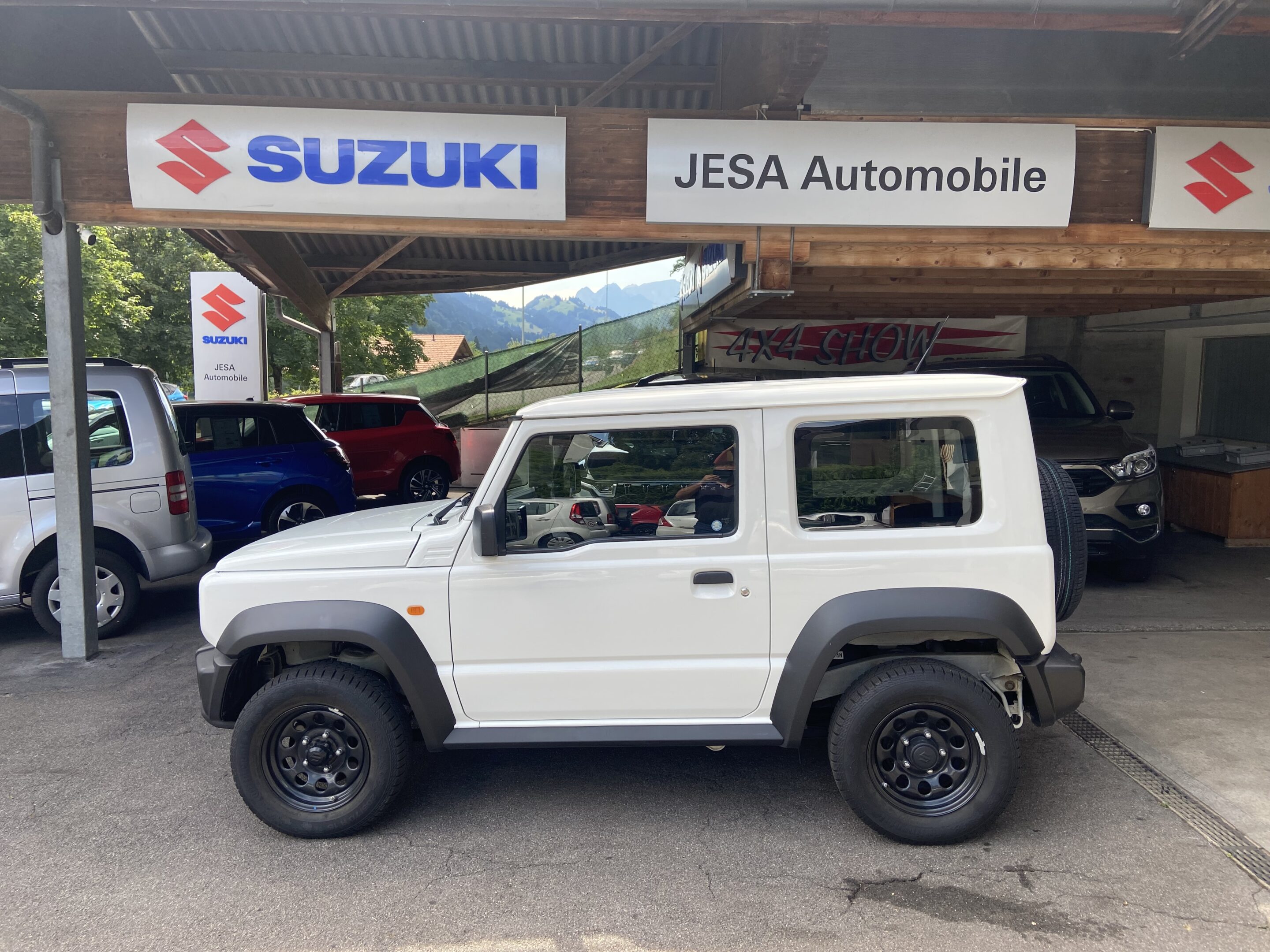 Weißer Suzuki Geländewagen bei JESA Automobile Ausstellungsraum, 4x4-Fahrzeuge im Hintergrund.