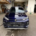 Blauer Suzuki vor einer Autowerkstatt mit Jesa Automobile-Schild im Hintergrund.