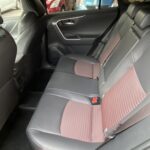 Rückbank eines Autos mit schwarzen Ledersitzbezügen und roten Akzenten, Autos im Hintergrund sichtbar.
