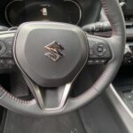 Lenkrad eines Suzuki-Autos mit Bedienelementen und roter Naht im Innenraum.