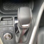 Automatikgetriebe mit Fahrmodus-Knopf in einem Fahrzeuginterieur mit schwarzem Leder und roten Nähten.