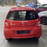 Roter Suzuki Alto, parkend auf einem Parkplatz mit verschneiten Bergen im Hintergrund.