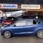 Blauer Suzuki vor Autohaus Jesa im Freien, mit mehreren anderen Suzuki-Modellen im Hintergrund, im Winter.