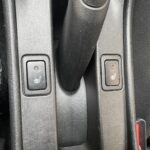 Schalter für Sitzheizung in einem Auto, links und rechts vom Schalthebel, auf einer schwarzen Konsole.