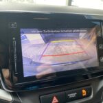 Rückfahrkamera-Bildschirm eines Autos, zeigt Parkbereich und Sicherheitswarnung beim Zurücksetzen.
