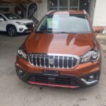 Roter Suzuki S-Cross in einem Autohaus, umgeben von weiteren Fahrzeugen.