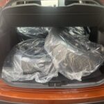 Kofferraum eines orangefarbenen Autos mit verpackten Autoreifen, bereit für den Transport.