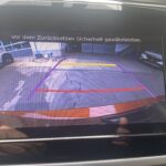 Rückfahrkamera-Display im Auto, zeigt Abstandslinien und Garageneinfahrt mit der Warnung, beim Zurücksetzen Sicherheit zu gewährleisten.