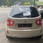 Kompakter beige Suzuki Ignis Hybrid, Heckansicht auf Parkplatz mit grüner Landschaft im Hintergrund.