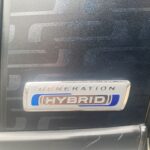 Hybrid-Autoemblem mit der Aufschrift Generation Hybrid auf einem blau-schwarzen Fahrzeughintergrund.