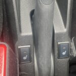 Schalter für Sitzheizung im Auto neben einem Sicherheitsgurtknopf in einer Nahaufnahme.