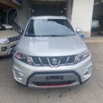 Silberner Suzuki SUV parkt vor einer Garage, links ist ein beige SUV sichtbar.