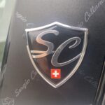 Logo auf einer Autotür mit Initialen SC und einem kleinen Schweizer Kreuz darunter.