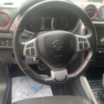 Lenkrad und Armaturenbrett eines modernen Suzuki-Autos mit rotem Akzent, Schaltknüppel und Touchscreen-Display.