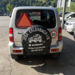 Autoheck mit Ersatzradabdeckung „Jesa Erlenbach“, Suzuki-Werkstatt. Parkplatz mit mehreren Autos im Hintergrund.