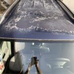 Autodach mit abblätterndem Lack; Innenansicht mit Spiegelung des Fotografen in der Windschutzscheibe.