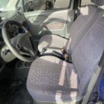Innenraum eines Autos mit zwei vorderen Stoffpolstersitzen und Lenkrad, beleuchtet durch Sonnenlicht.