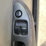 Nahaufnahme von Fensterhebern und Türöffner in einem Auto, schwarze Knöpfe auf dunkelgrauem Hintergrund.