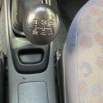 Gangschaltung eines Autos mit fünffachem Schaltschema, schwarzer Knauf und grauem Sitzelement im Hintergrund.