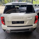 Rückansicht eines weißen SUVs mit dem Schriftzug Torres auf einem Parkplatz vor einer grünen Berglandschaft.