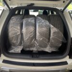 Vier Autoreifen in Plastikhüllen im Kofferraum eines SUVs, bereit für den Transport.