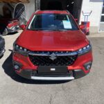 Roter Suzuki SUV vor einem Autohändler, vorne fotografiert bei sonnigem Wetter.