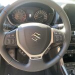 Lenkradansicht eines Suzuki-Autos mit integriertem Bedienfeld und Tachometer bei Tageslicht.