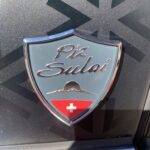 Logo von Piz Sulai mit dem Schweizer Kreuz auf schwarzer Oberfläche, Symbol für Schweizer Auto oder Marke.