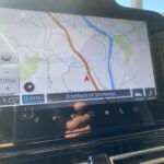 Navi zeigt Erlenbach im Simmental auf Touchscreen im Auto bei sonnigem Wetter an.