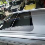 Eine Reihe moderner Autos in einem Autohaus, mit einem silberfarbenen Fahrzeug im Vordergrund unter einem Glasdach.