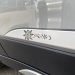 Autoaufkleber mit Blumenmotiv auf grauer Fahrzeugtür, dekorativer Akzent eines Autos.